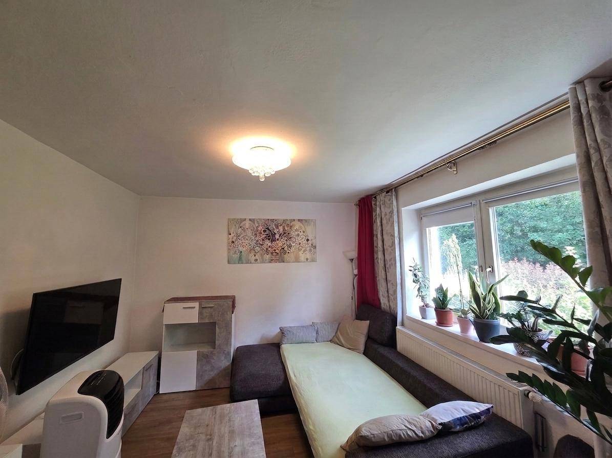 Helles Wohnzimmer mit Sofa, Fernseher und Blick auf die grüne Umgebung.