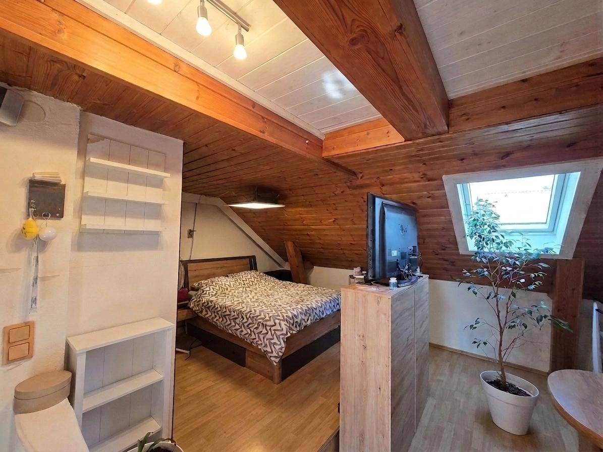 Gemütliches Schlafzimmer im Dachgeschoss mit Holzbalkendecke und Dachfenster.