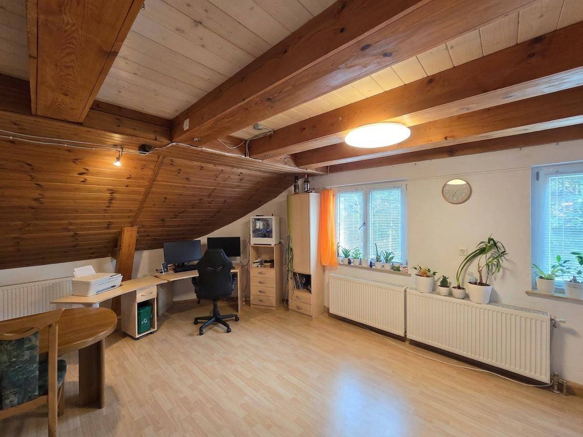 Helles Büro im Dachgeschoss mit Holzbalkendecke, Schreibtisch und Fenstern.