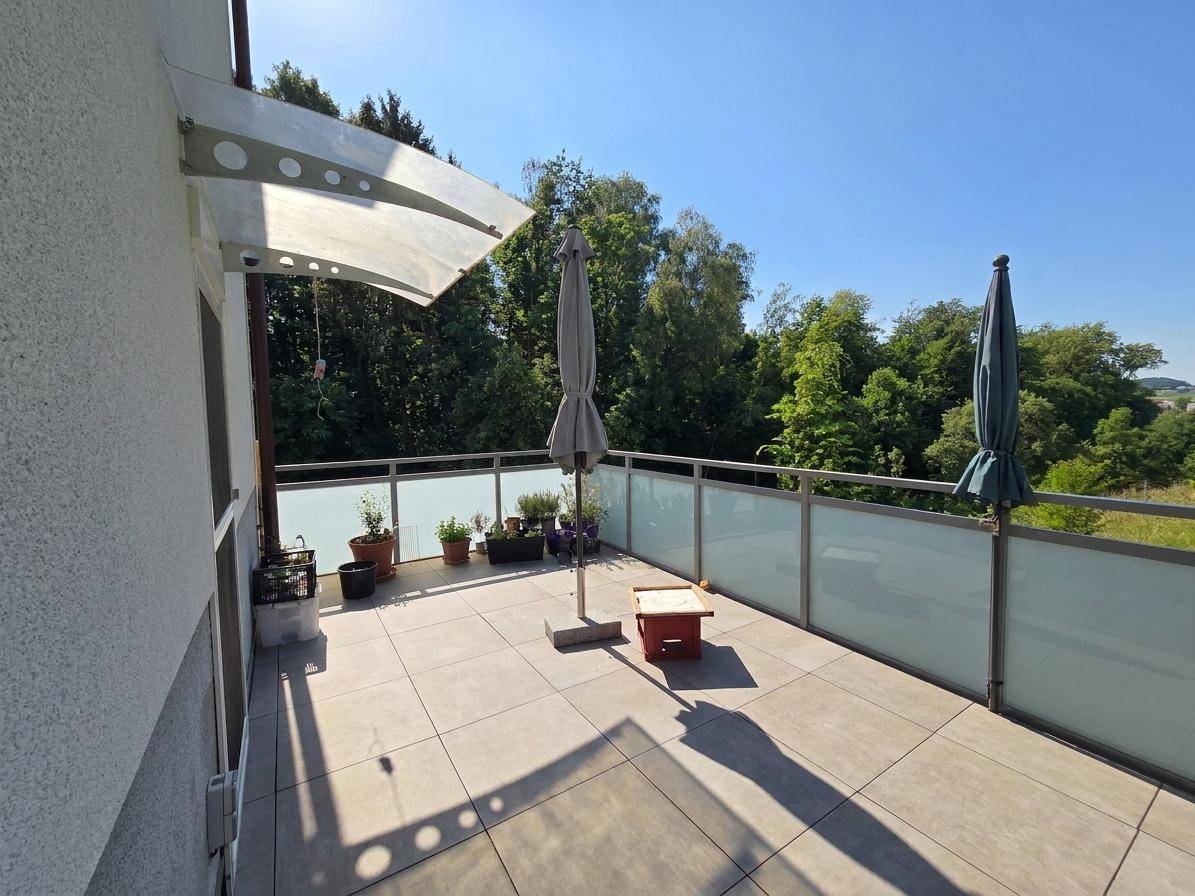 Geräumiger Balkon mit Fliesenboden, Sonnenschirmen und weitem Blick ins Grüne.