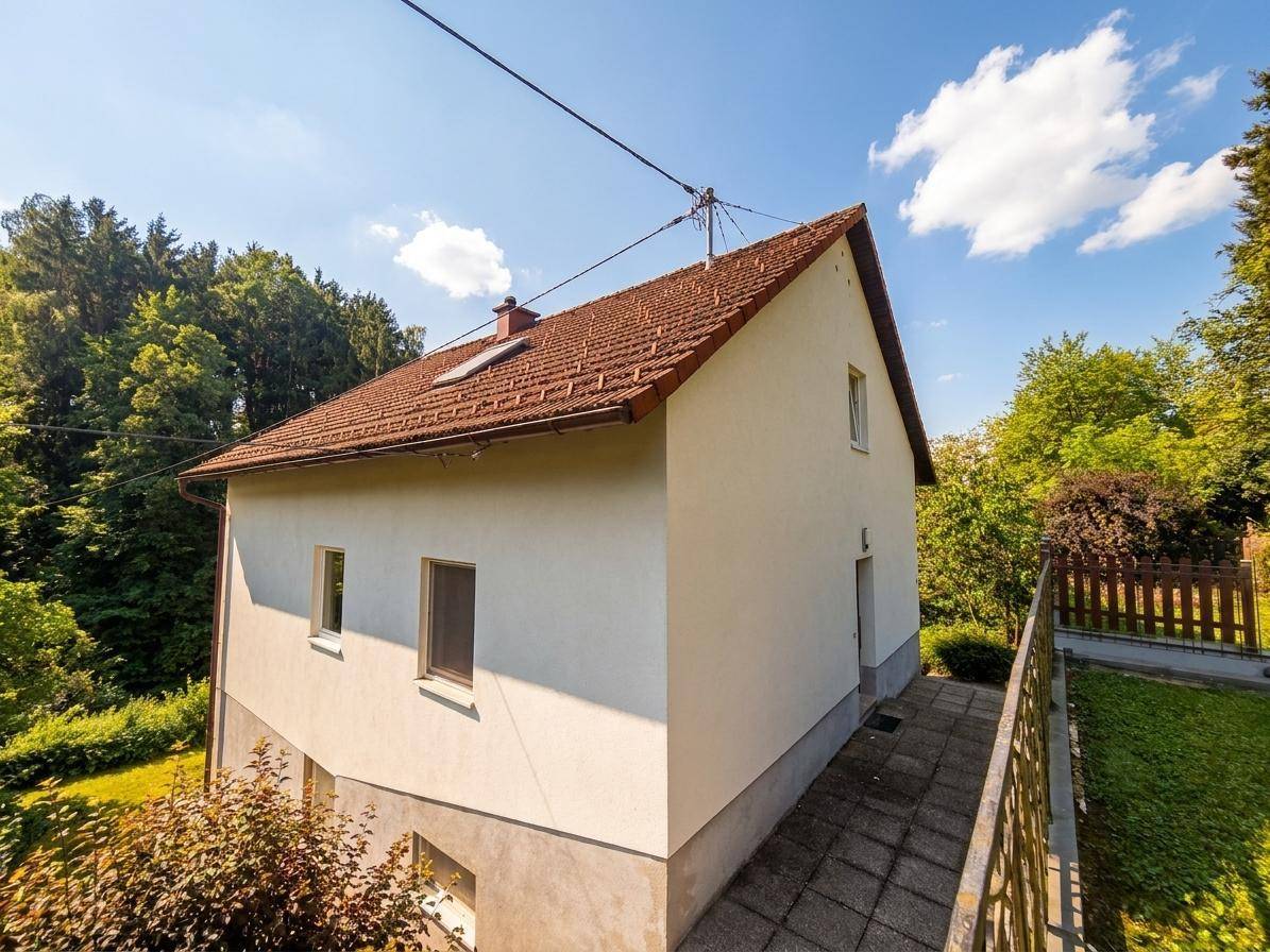 Seitenansicht des Hauses mit ziegelgedecktem Satteldach und umgebender Natur.