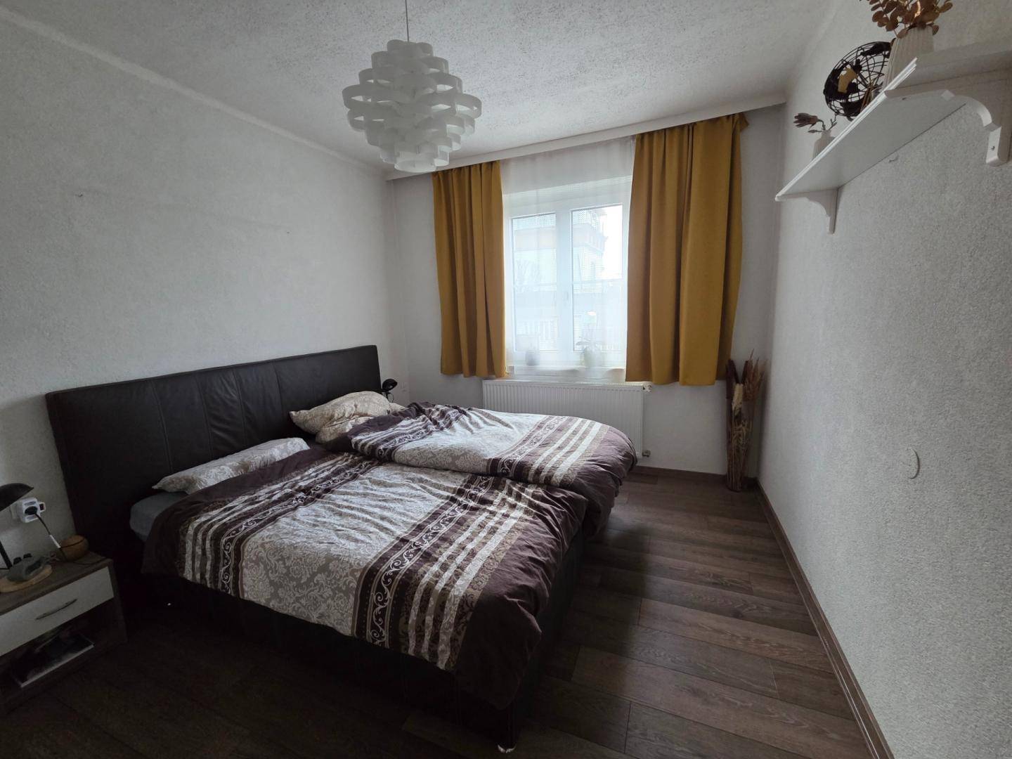 Schlafzimmer mit Holzboden, Doppelbett und gelben Vorhängen am Fenster.