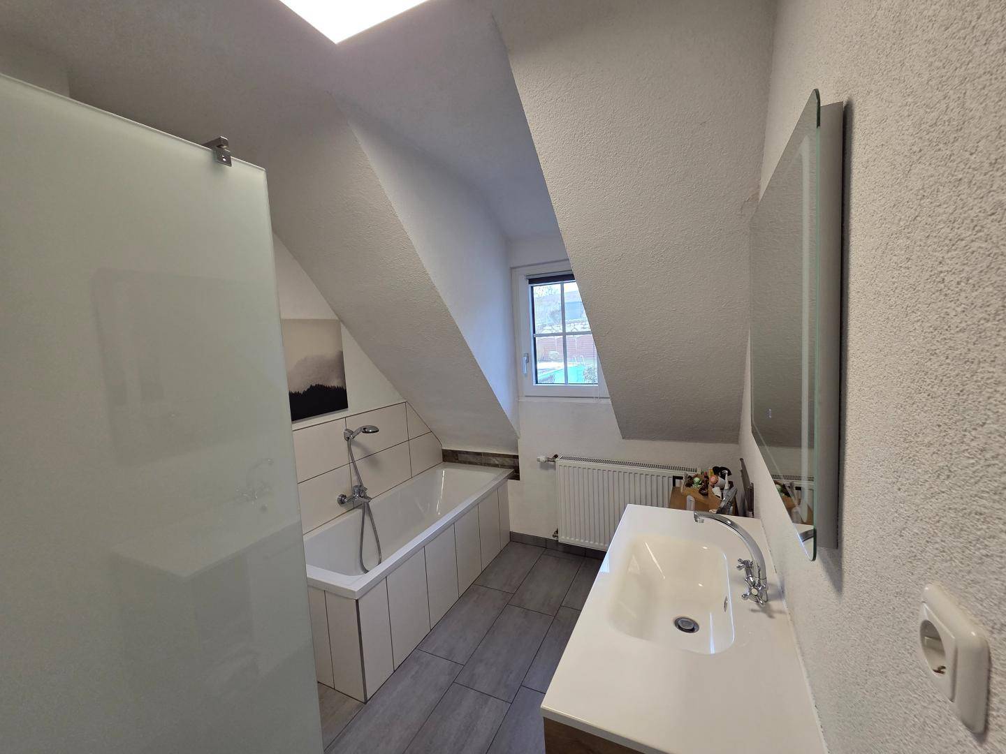 Badezimmer im Dachgeschoss mit Badewanne, Waschbecken und Dachfenster.
