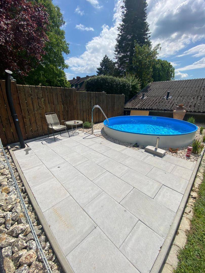 Gepflasterte Terrasse mit Aufstellpool, Außendusche und Sitzgelegenheiten.