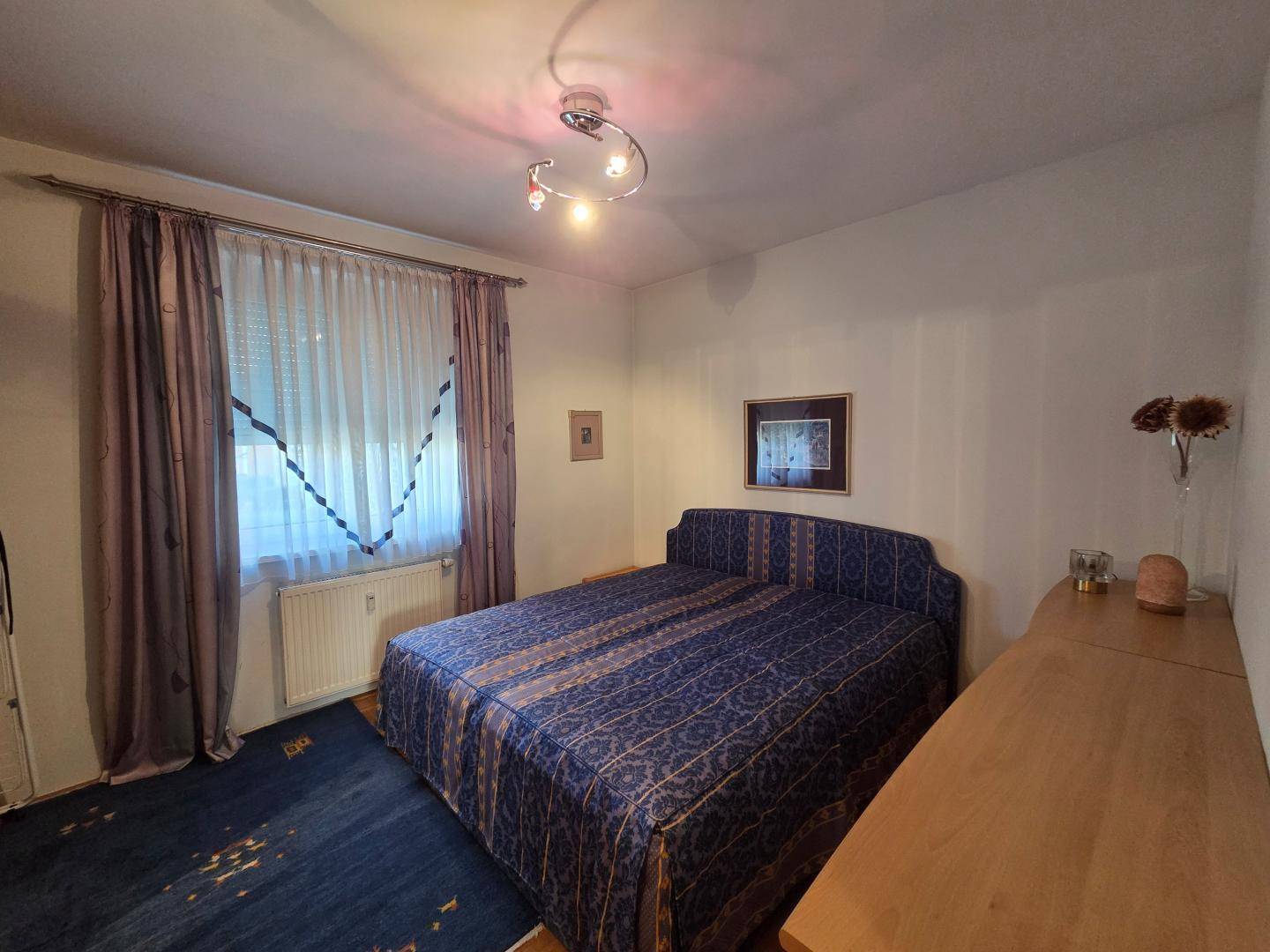 Schlafzimmer mit Doppelbett, Teppichboden und Vorhängen, bietet eine ruhige Rückzugsmöglichkeit.