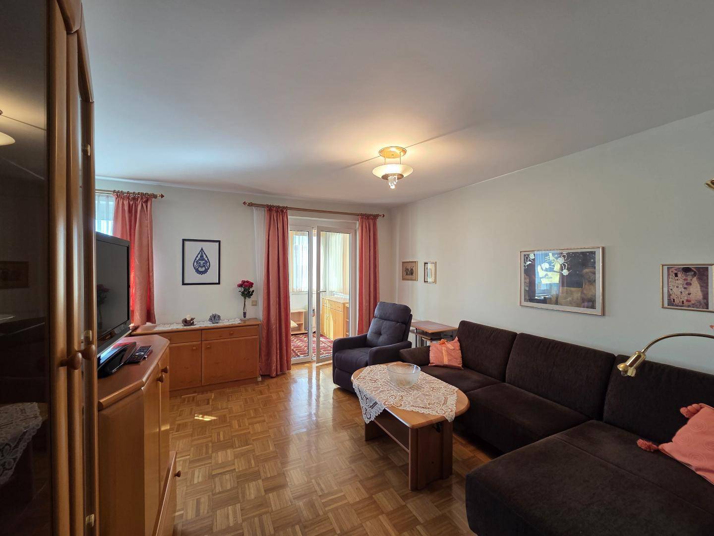 Gemütliches Wohnzimmer mit Parkettboden, dunklem Sofa und Zugang zu einem Balkon.