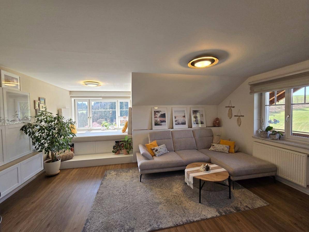 Gemütliches Wohnzimmer mit Sofa, Teppich und einer erhöhten Fenstersitzbank mit Ausblick.