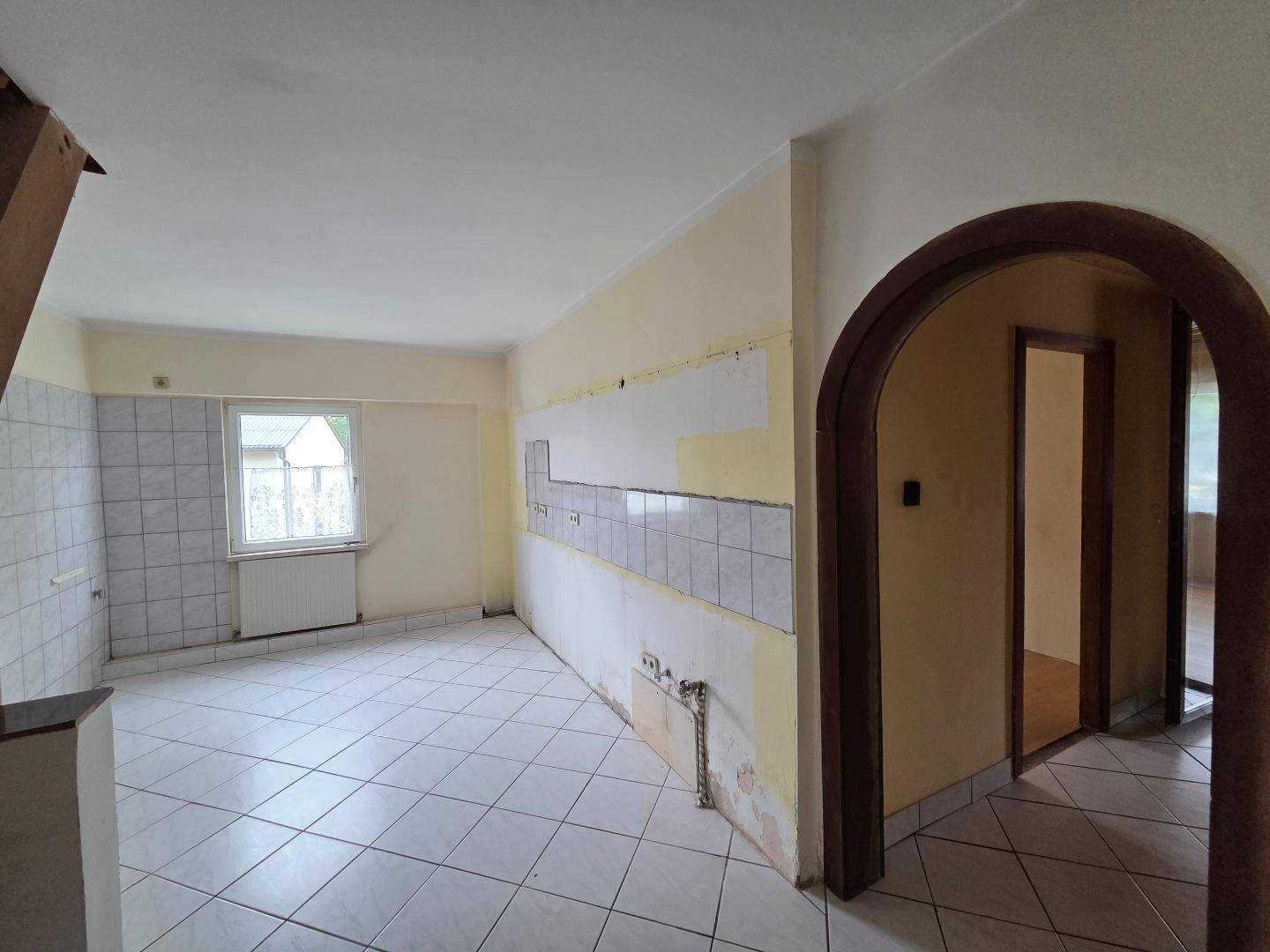 Leere Küche mit Fliesenboden, Fenster und vorbereiteten Wänden für die Installation einer Einbauküche.