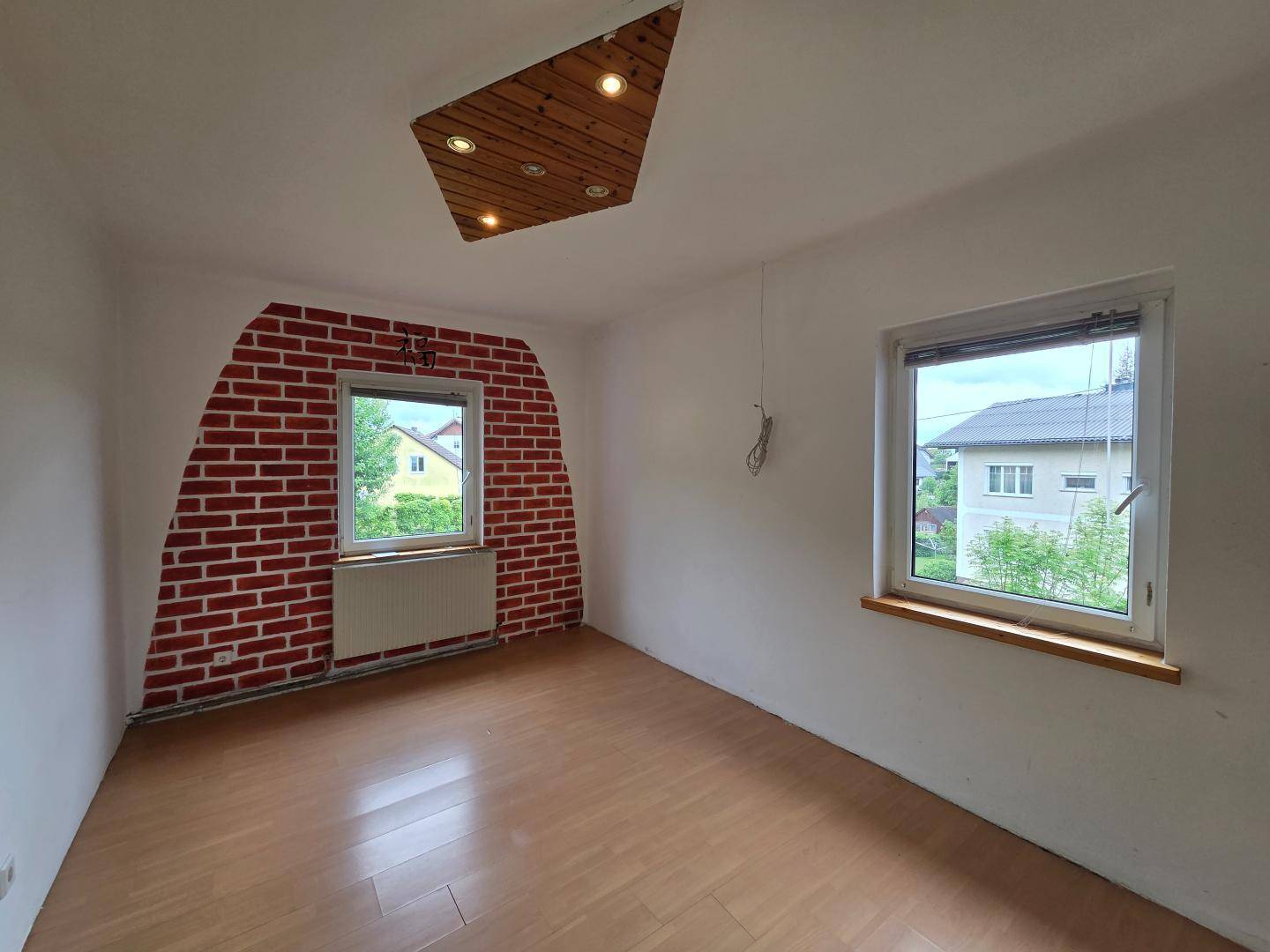 Kinderzimmer mit Ziegelwandakzent, Holzboden und zwei Fenstern, bereit zur Gestaltung.