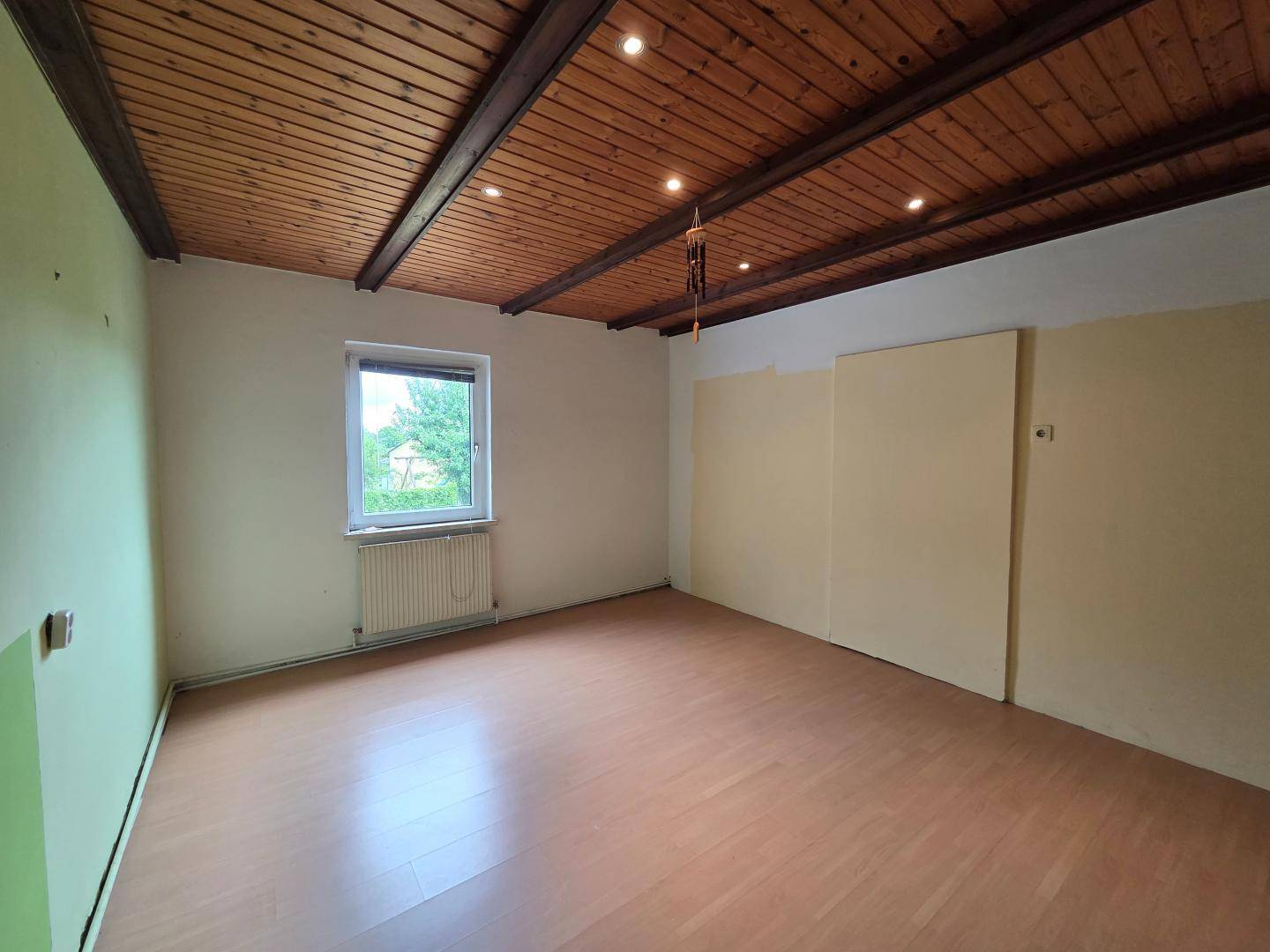 Schlafzimmer mit Holzbalkendecke, Laminatboden und einem Fenster mit Blick ins Grüne.
