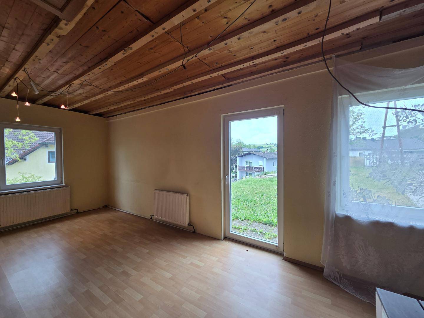 Geräumiges Zimmer mit Holzbalkendecke, Laminatboden und Zugang zum Außenbereich.