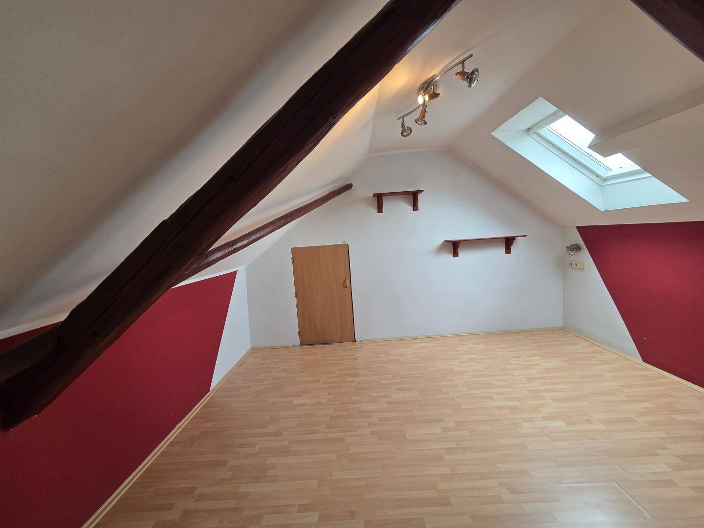 Dachzimmer mit sichtbaren Holzbalken, Dachfenster und roten Akzentwänden, bereit zur Einrichtung.