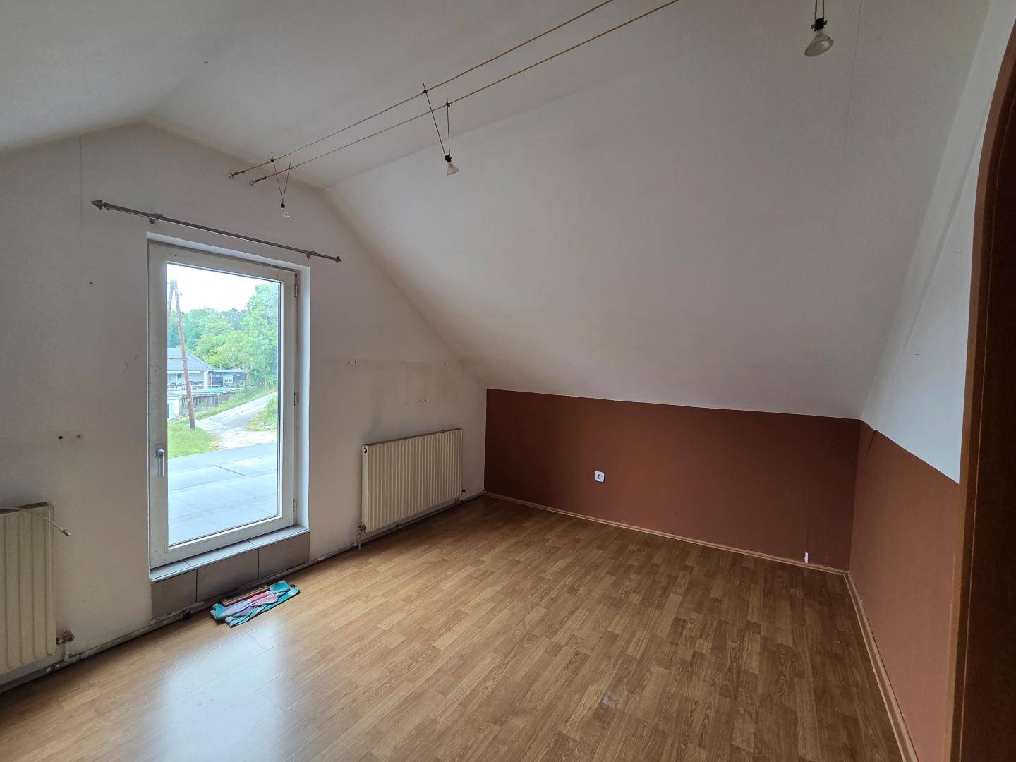 Leeres Zimmer im Dachgeschoss mit Dachschräge, Laminatboden und großem Fenster zur Straße.