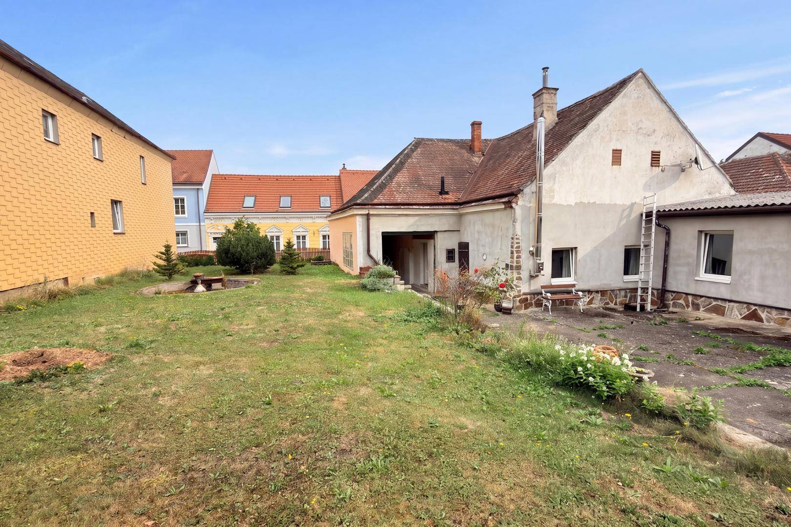 Großer Gartenbereich hinter dem Haus mit Rasenfläche, Bäumen und Blick auf die Rückseite des Gebäudes.