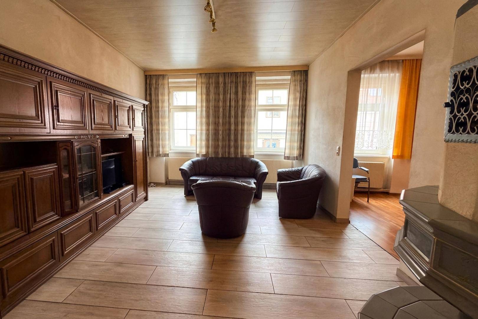 Gemütliches Wohnzimmer mit traditionellen Holzmöbeln, Ledersofas und einem Kachelofen als Blickfang.