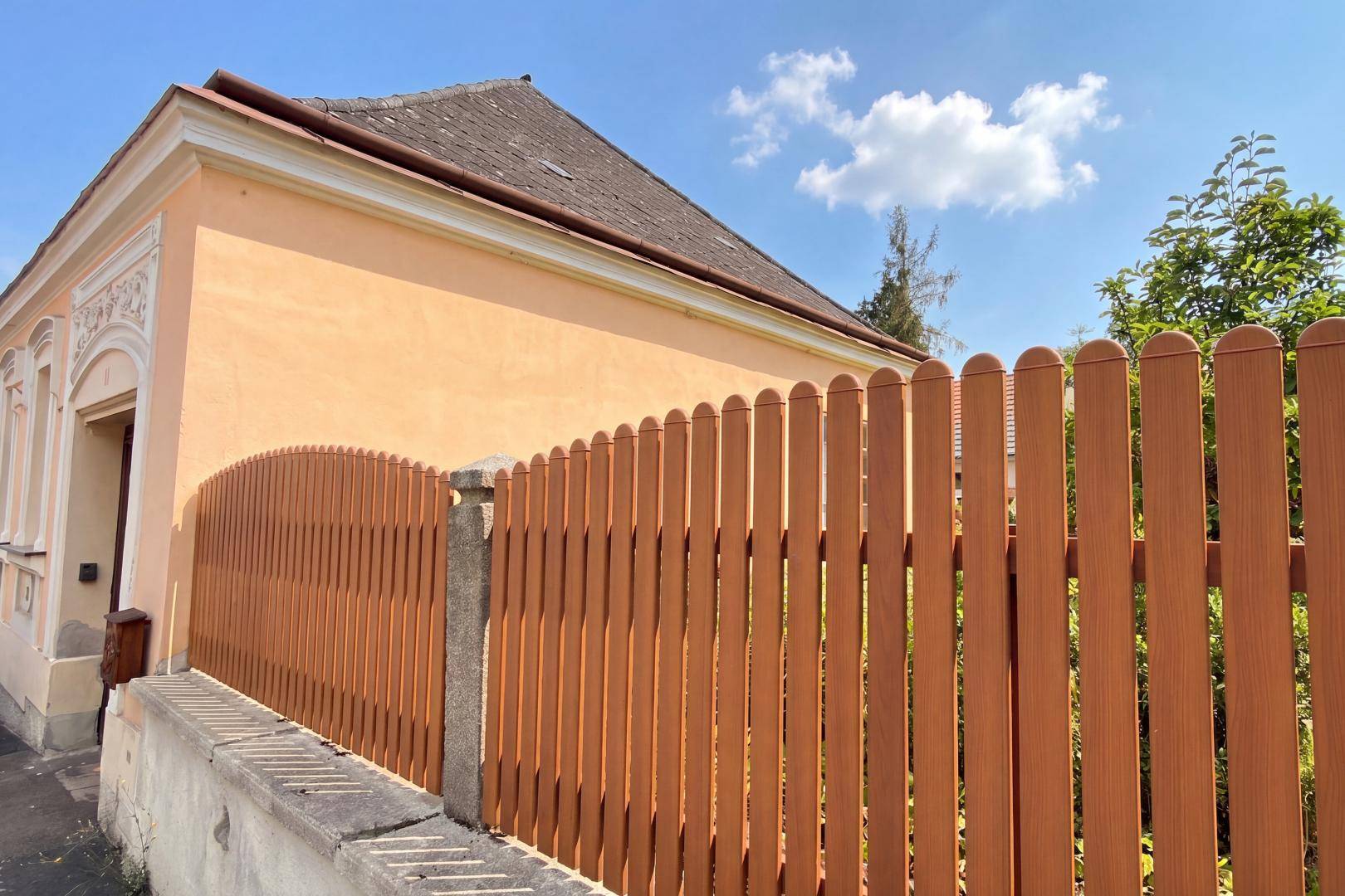 Seitenansicht des Hauses mit einem neuen Holzzaun und traditioneller Architektur unter klarem Himmel.