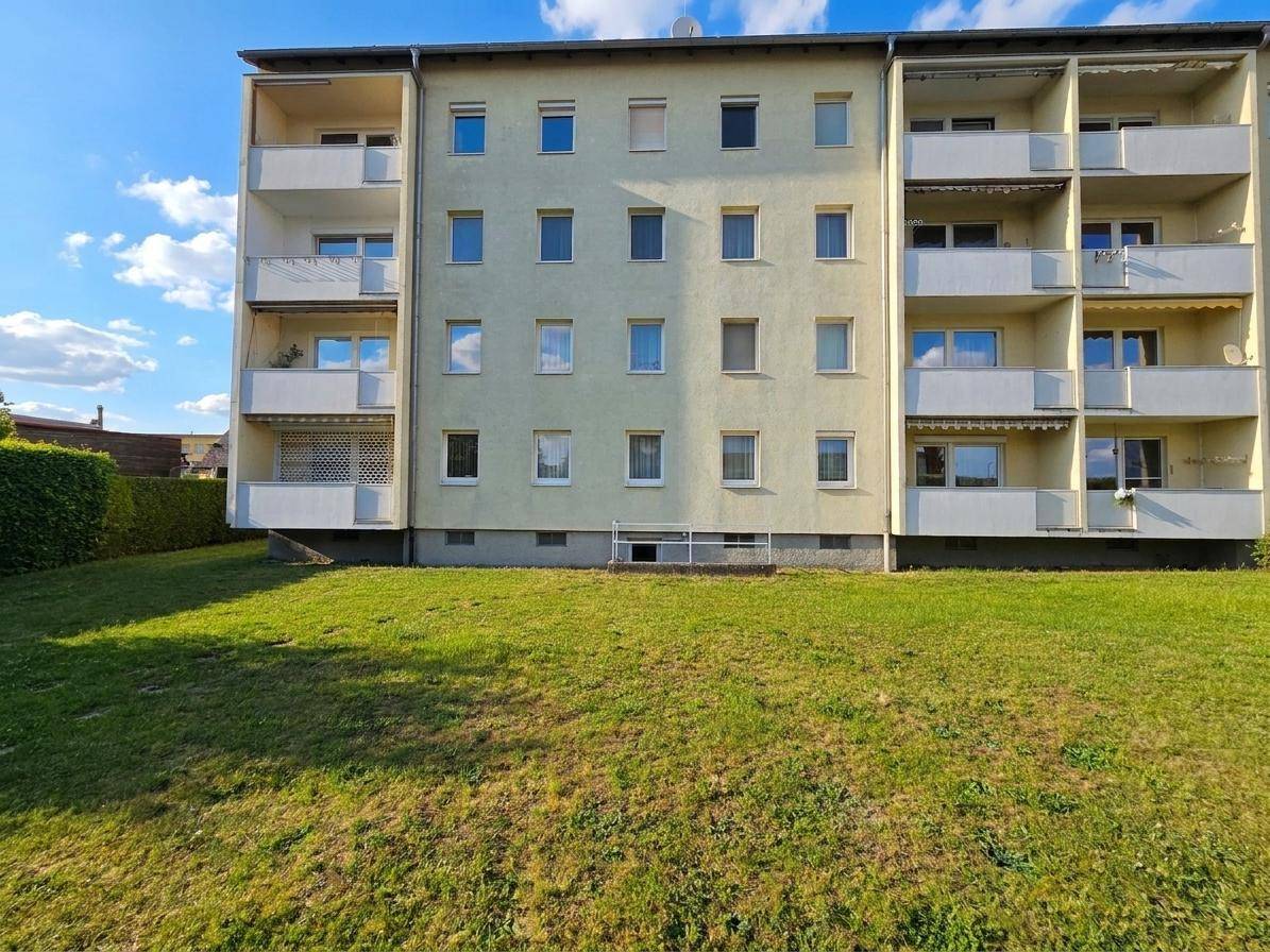 Mehrfamilienhaus mit Balkonen und einer großen Rasenfläche im Vordergrund an einem sonnigen Tag.