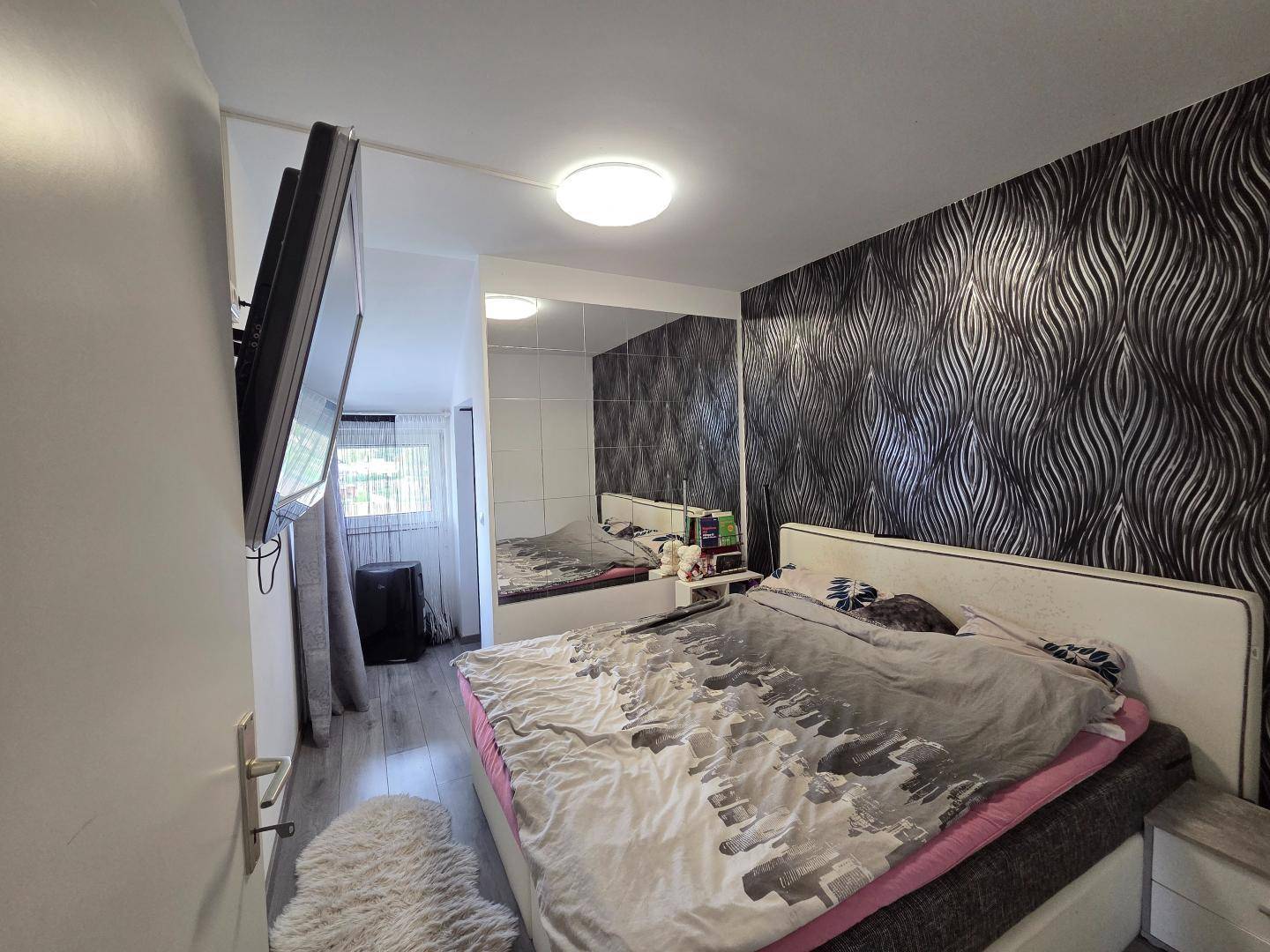 Schlafzimmer mit dunkler Mustertapete, Spiegelfronten und hellem Laminatboden.