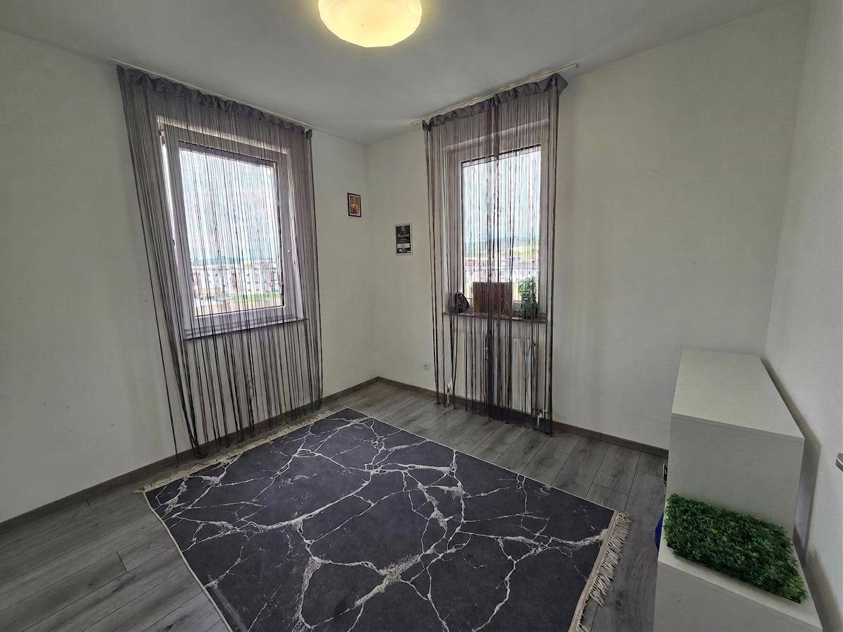Helles Zimmer mit zwei Fenstern und grauem Laminatboden, vielseitig nutzbar.