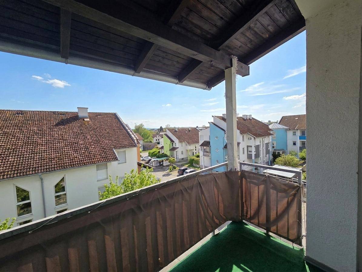 Überdachter Balkon mit Blick auf die umliegenden Häuser und grüne Landschaft.