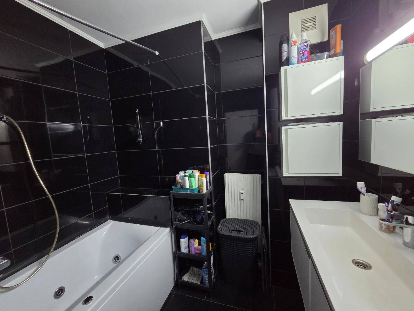 Modernes Badezimmer mit schwarzen Fliesen, Badewanne mit Whirlpoolfunktion und Einzelwaschbecken.