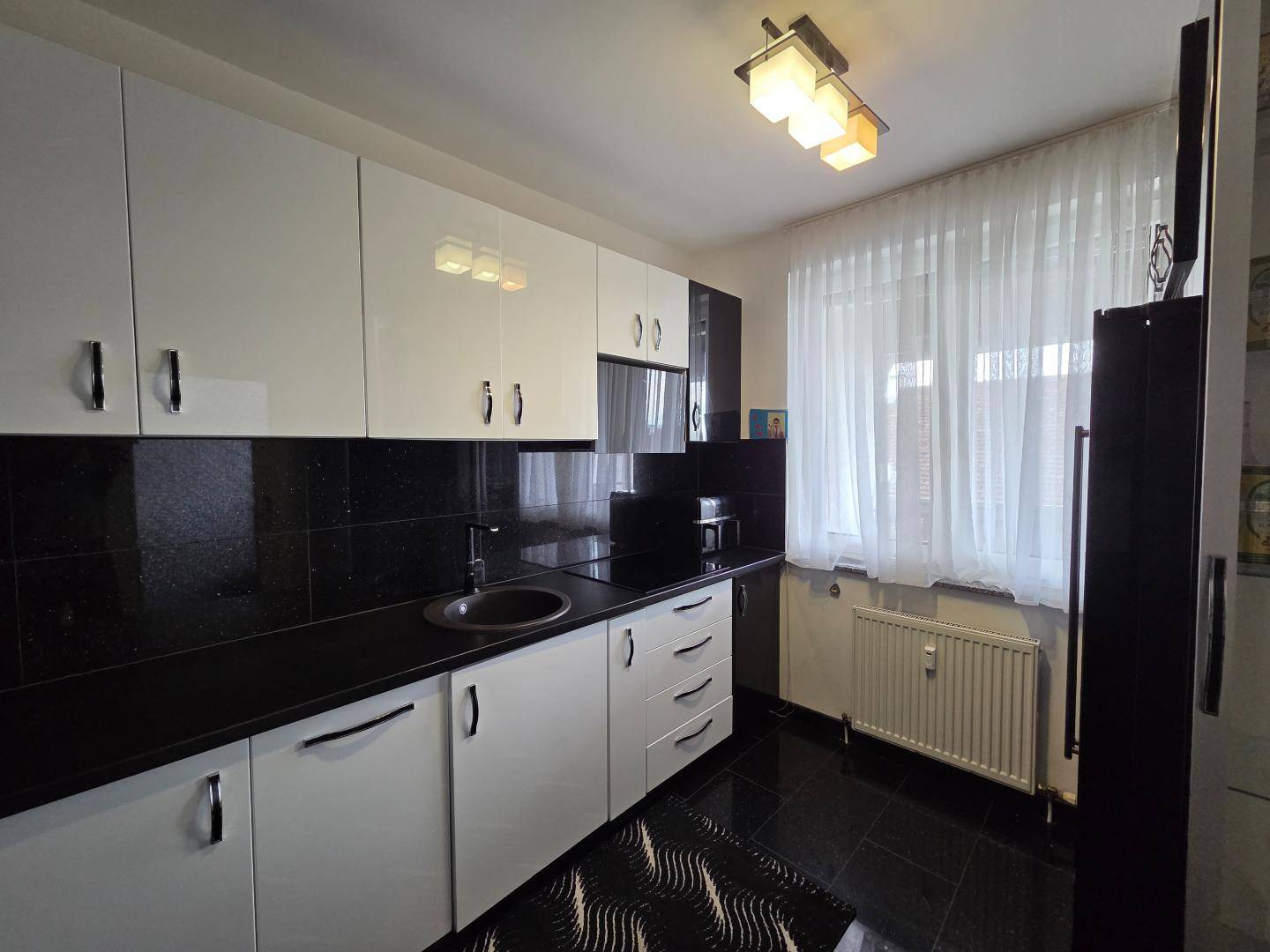 Moderne Küche mit weißen Hochglanzschränken, schwarzen Arbeitsplatten und Fliesenboden.