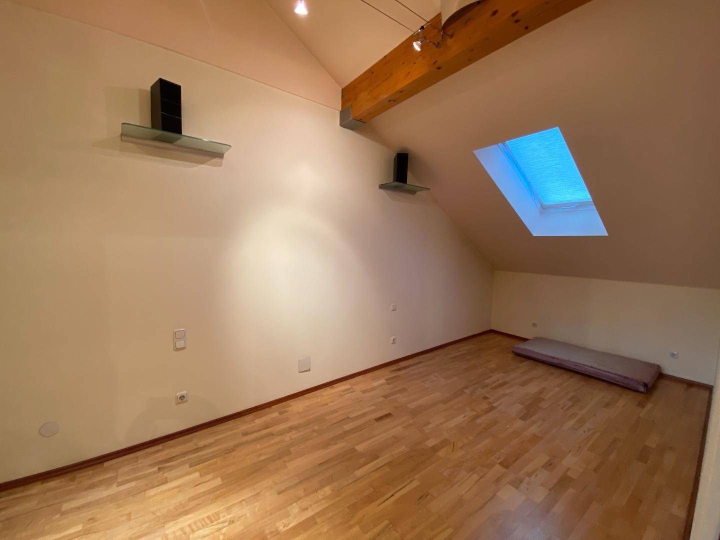 Dachgeschosszimmer mit Holzboden, sichtbaren Holzbalken und einem Dachfenster.