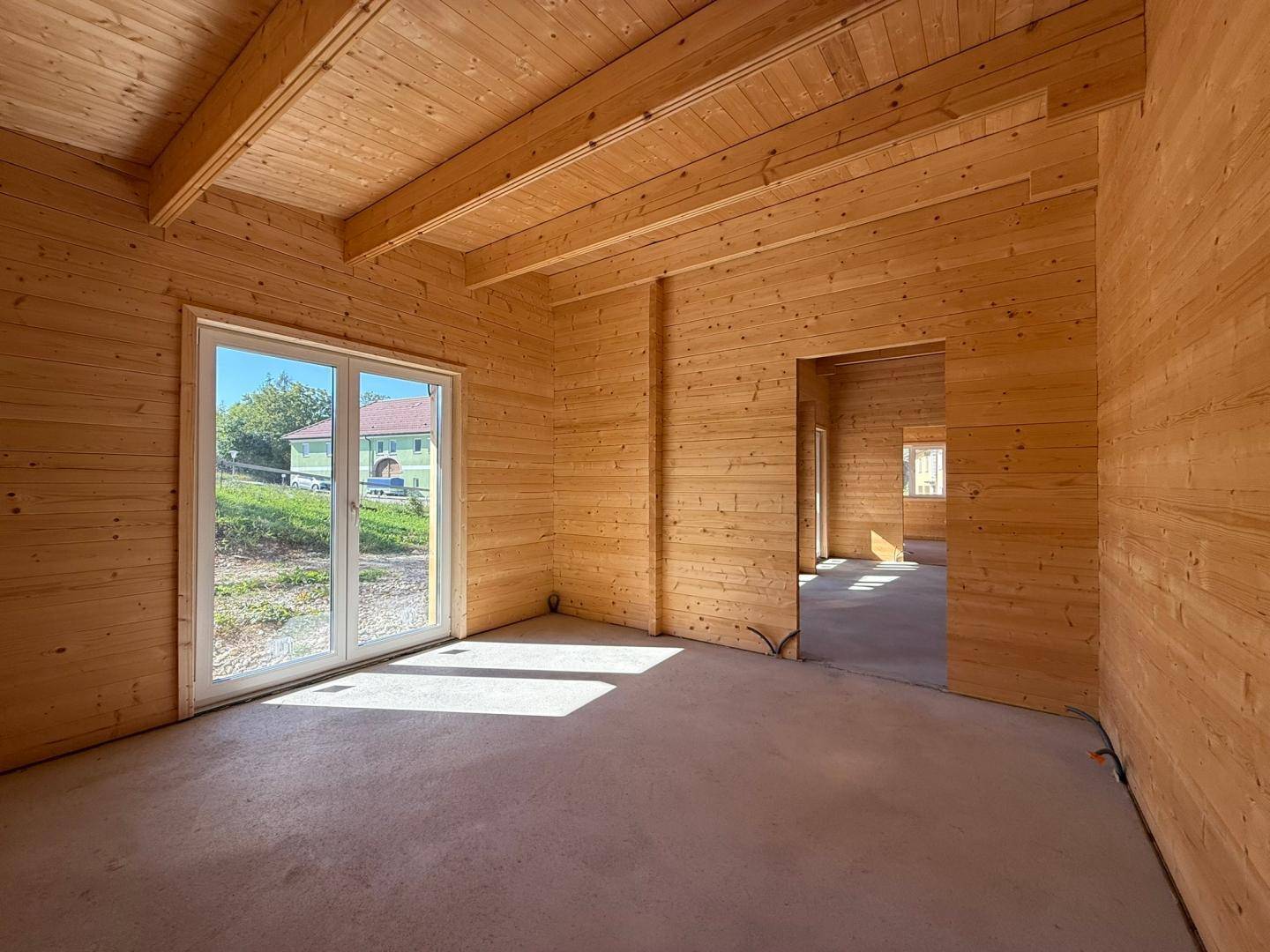 Unfertiger Raum mit Holzwänden, sichtbaren Deckenbalken und einem großen Fenster mit Blick nach draußen.