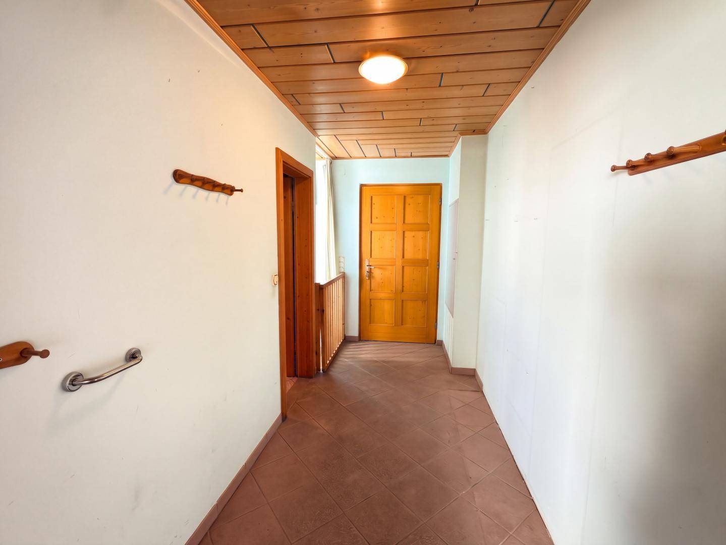 Flur mit Holzdecke, braunen Fliesen und Holztüren, ausgestattet mit Haltegriffen.