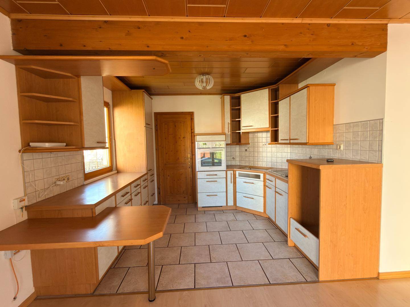 Küche mit Holzschränken, gefliestem Boden und sichtbaren Holzbalken an der Decke.