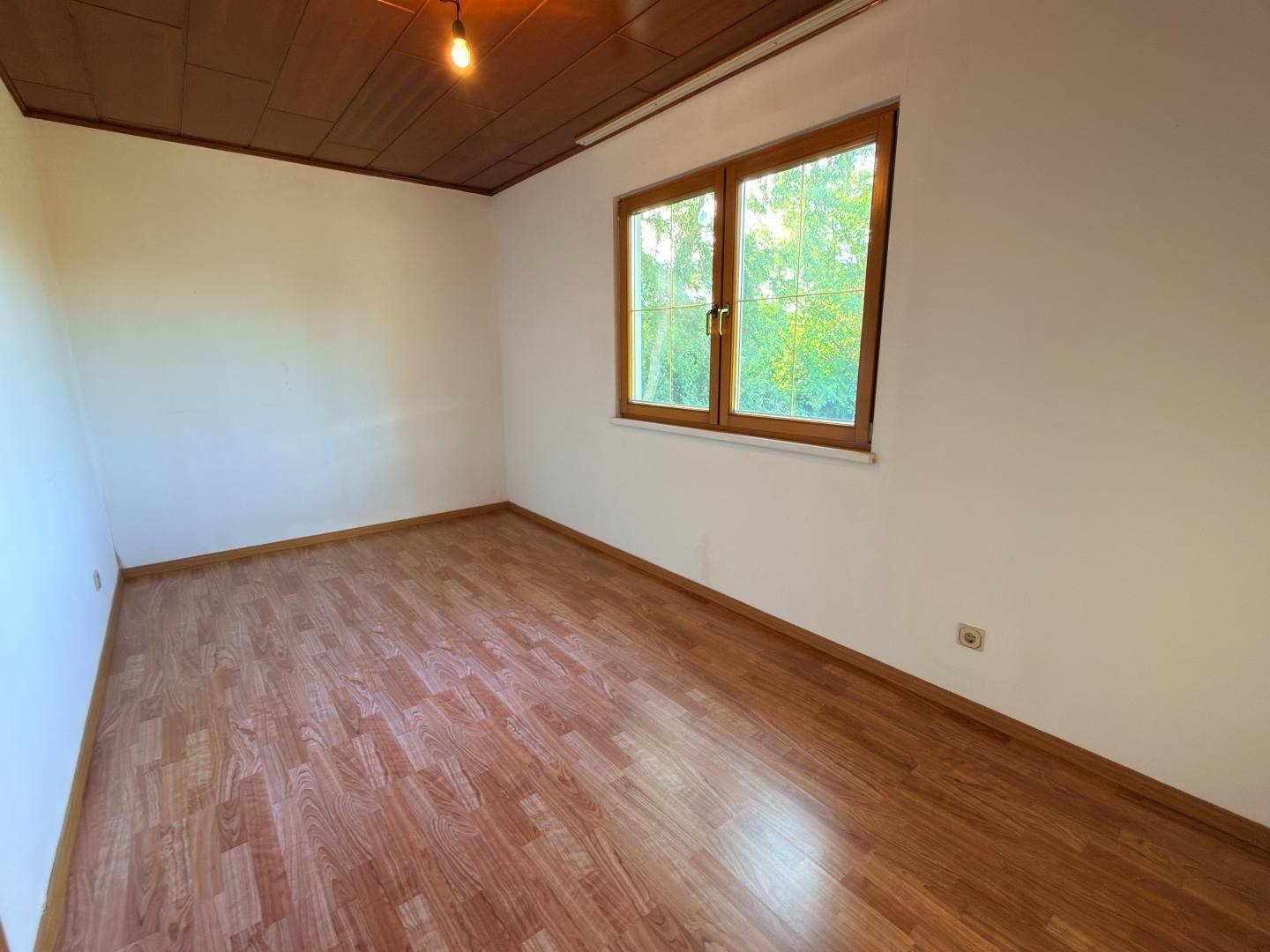 Helles Zimmer mit Holzdecke, Holzboden und Blick ins Grüne durch das Fenster.