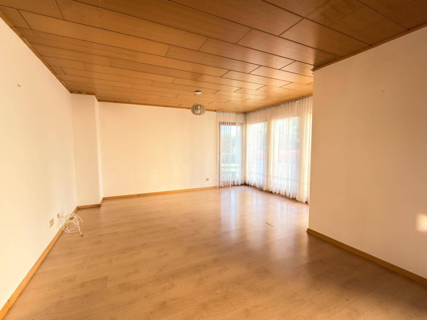 Geräumiges Wohnzimmer mit Holzdecke, hellem Parkettboden und großen Fenstern.
