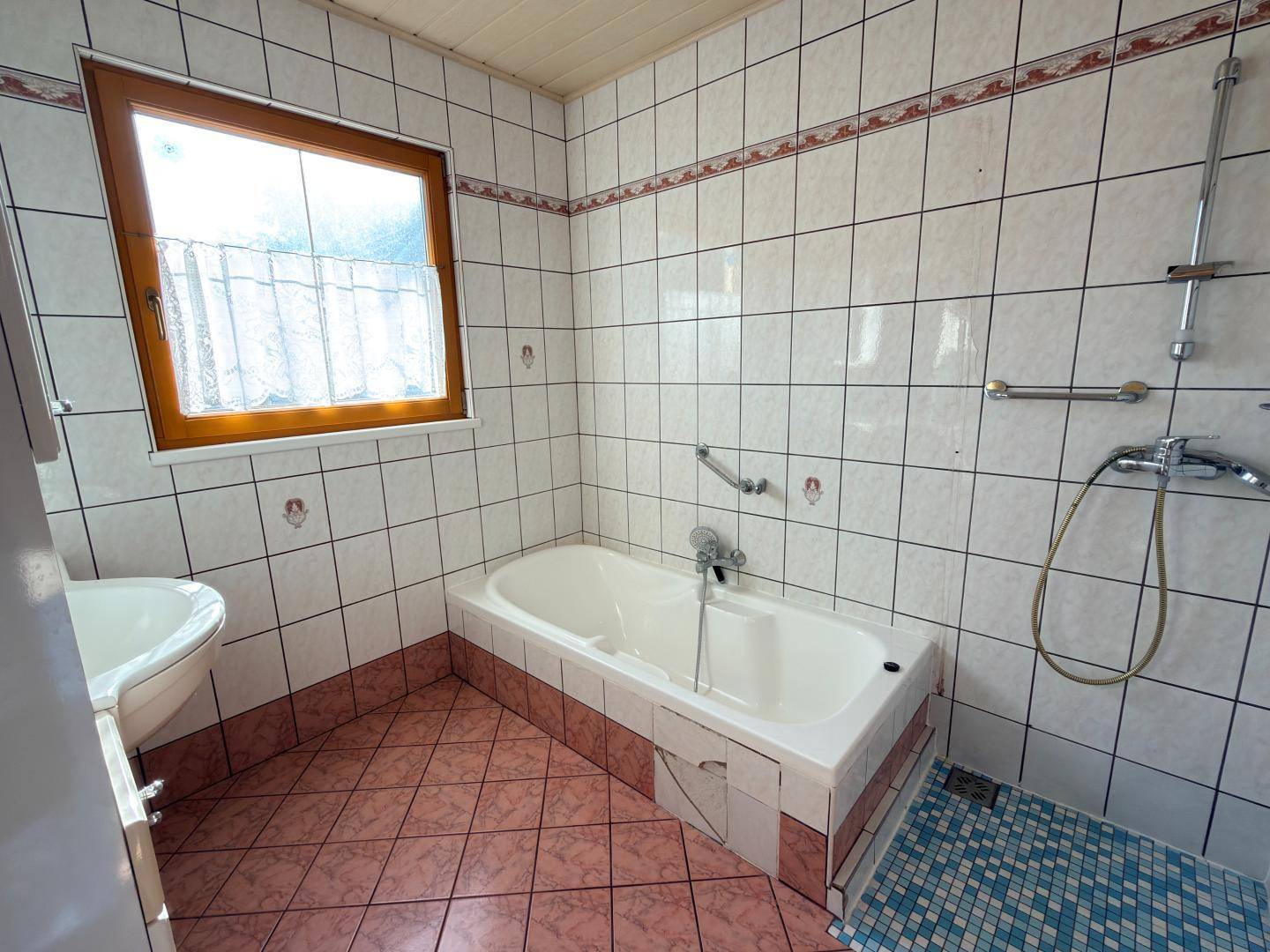 Badezimmer mit rosa-weißen Fliesen, Badewanne, Waschbecken und Fenster.