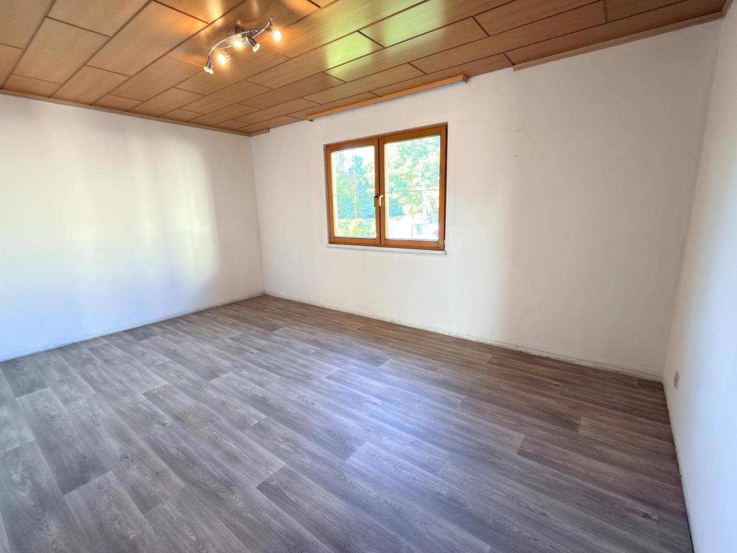 Geräumiges Schlafzimmer mit Holzdecke, grauem Laminatboden und Fenster.