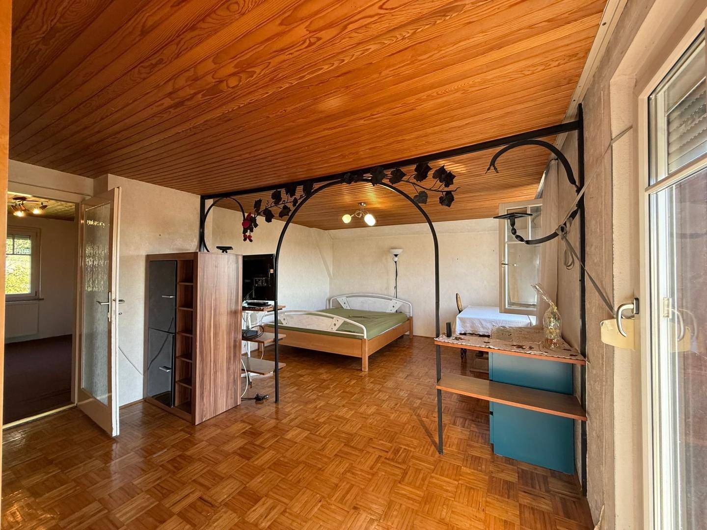 Schlafzimmer mit Holzdecke, Parkettboden und Zugang zum Balkon.
