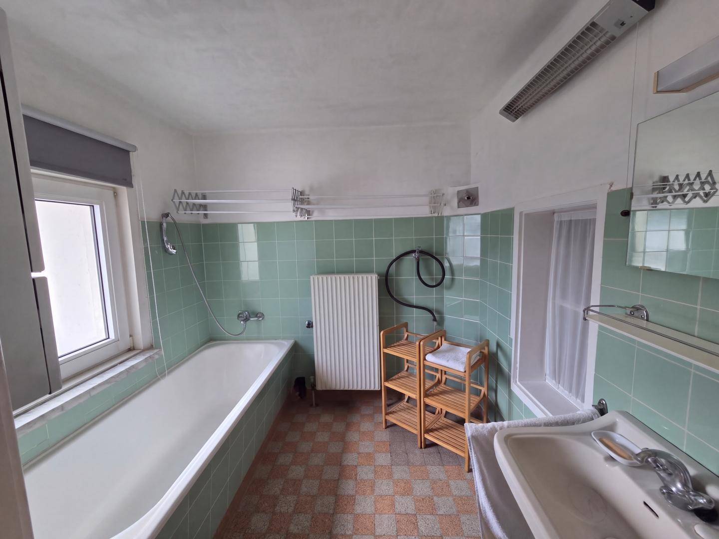 Badezimmer mit Badewanne, Waschbecken und grünen Wandfliesen im 80er-Jahre-Stil.