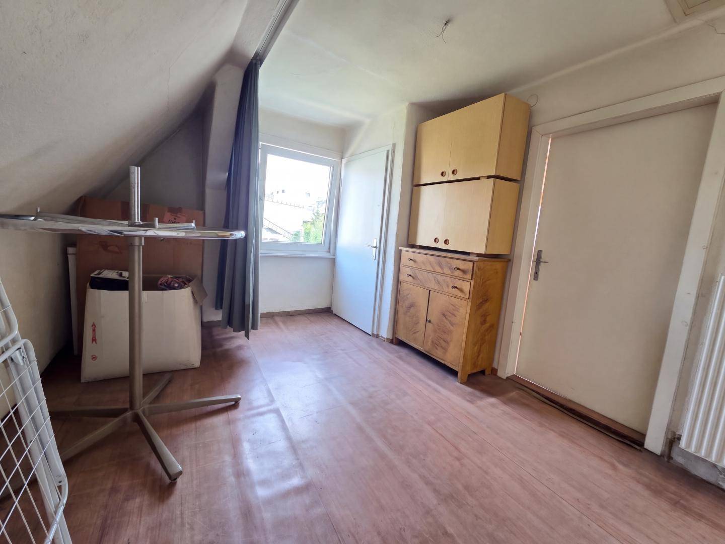 Dachgeschossraum mit schräger Decke, Fenster und Stauraum.