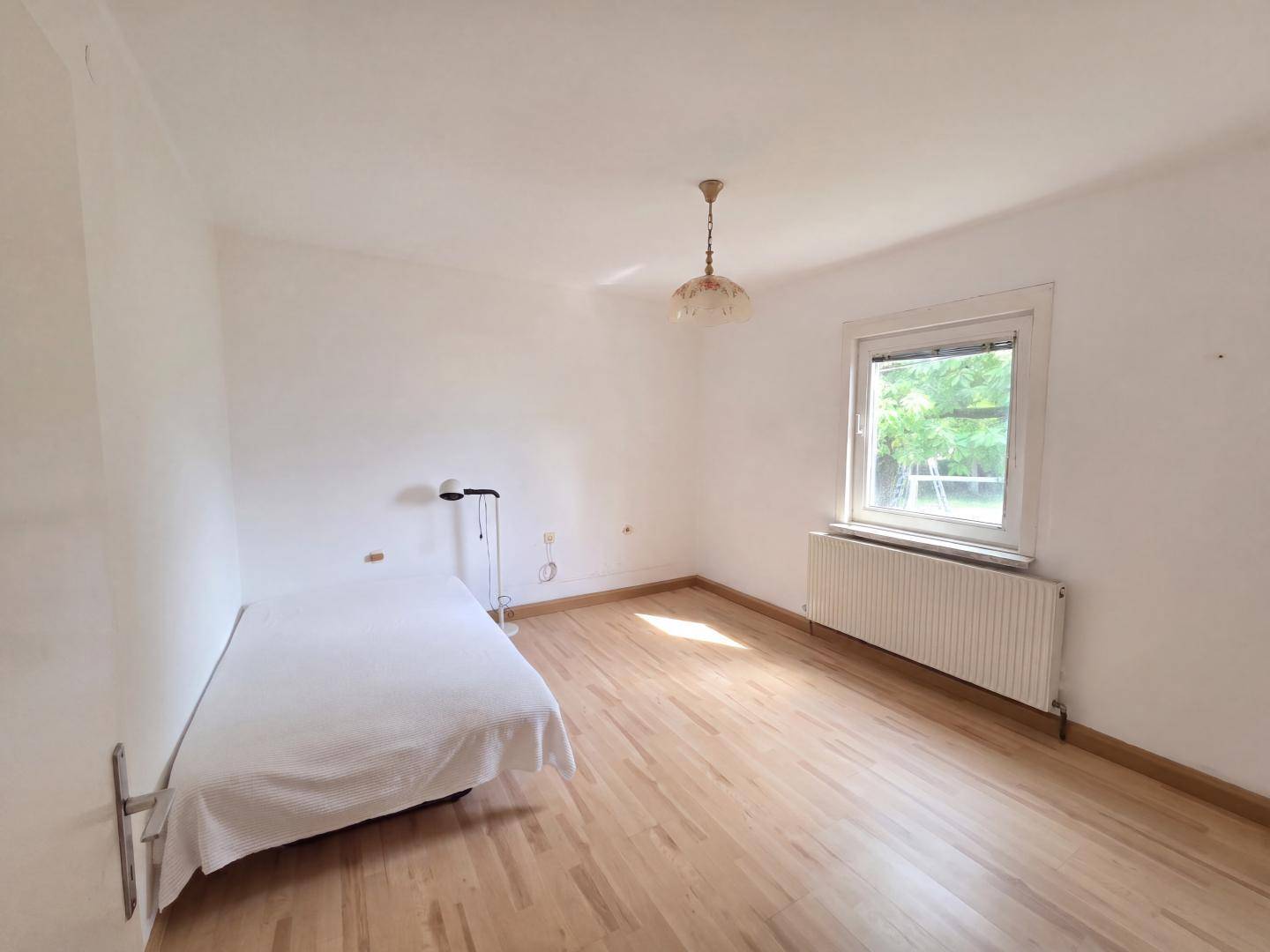 Helles Schlafzimmer mit Einzelbett, Parkettboden und Blick ins Grüne.