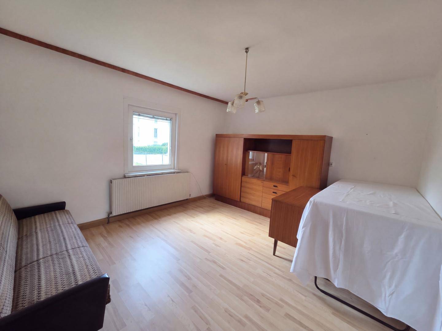 Schlichter Wohnraum mit Holzmöbeln, Sofa und hellem Laminatboden.