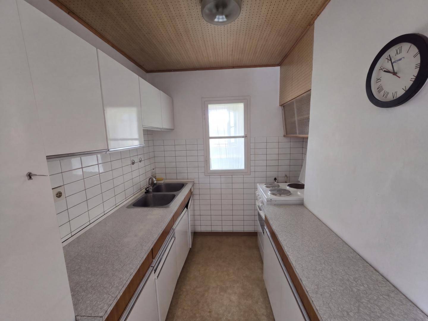 Schmale Küche mit weißen Oberschränken, Fliesenrückwand und älterem Herd.