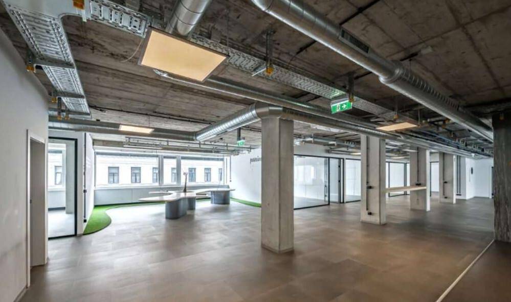 Großes, offenes Büro mit Sichtbetondecke, freiliegenden Rohren und großen Fenstern mit Stadtblick.