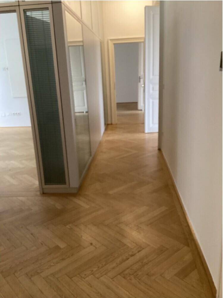 Langer Flur mit Fischgrätparkett, weißen Wänden und Türen zu angrenzenden Räumen.