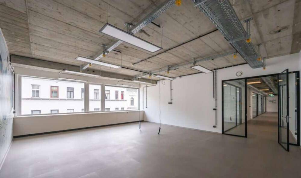 Helles Büro mit großen Fenstern, Sichtbetondecke und freiliegenden Lüftungsrohren im Industriestil.