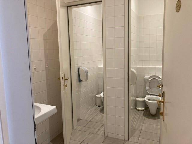 Öffentlicher Toilettenbereich mit mehreren Kabinen, weißen Fliesenwänden und einem kleinen Waschbecken.