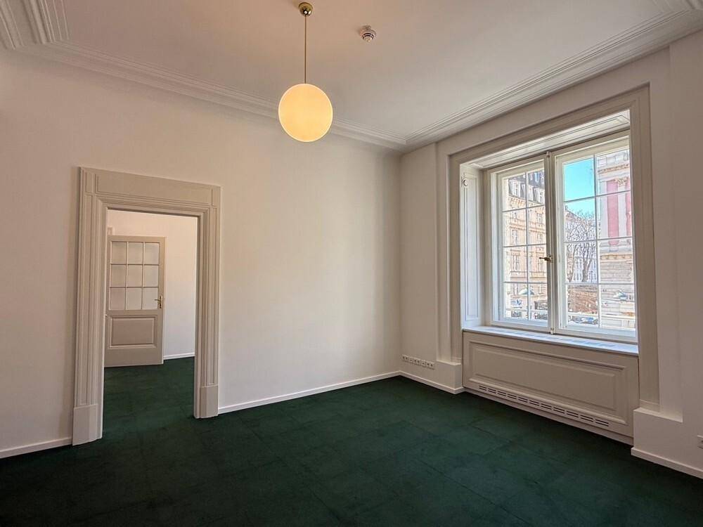 Büro mit grünem Teppichboden, weißen Wänden und einem großen Fenster, das den Raum mit Licht füllt.