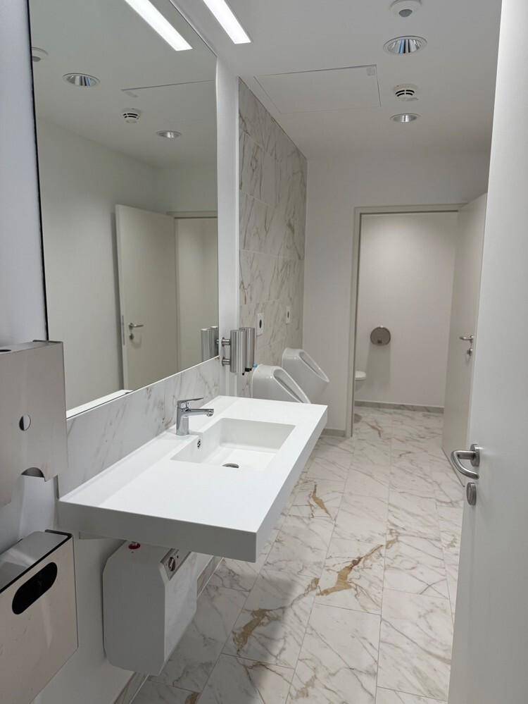Helles Badezimmer mit Marmorfliesen, Doppelwaschbecken und Urinal, das einen modernen Eindruck macht.