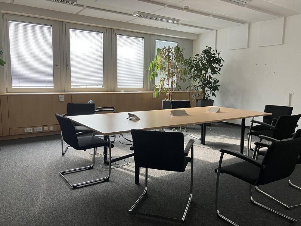 Konferenzraum mit langem Tisch und Bürostühlen, großen Fenstern und Pflanzen für eine angenehme Atmosphäre.