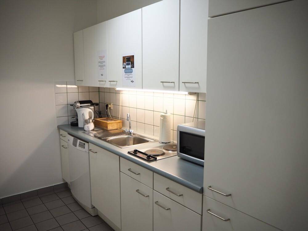 Kleine, funktionale Küchenzeile mit weißen Schränken, Spüle, Mikrowelle und Kochplatte für den täglichen Gebrauch.