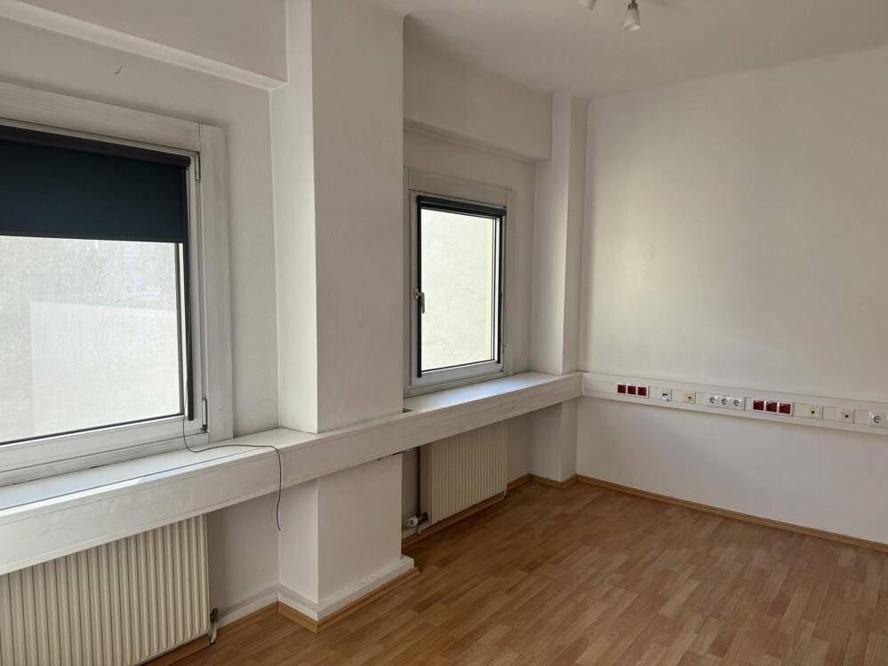 Geräumiger Büroraum mit hellen Wänden, Laminatboden und mehreren Fenstern für viel Licht.