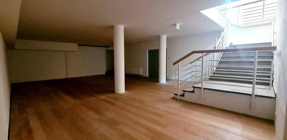 Geräumiger, heller Gewerberaum mit Holzfußboden, weißen Wänden und einer breiten Treppe.